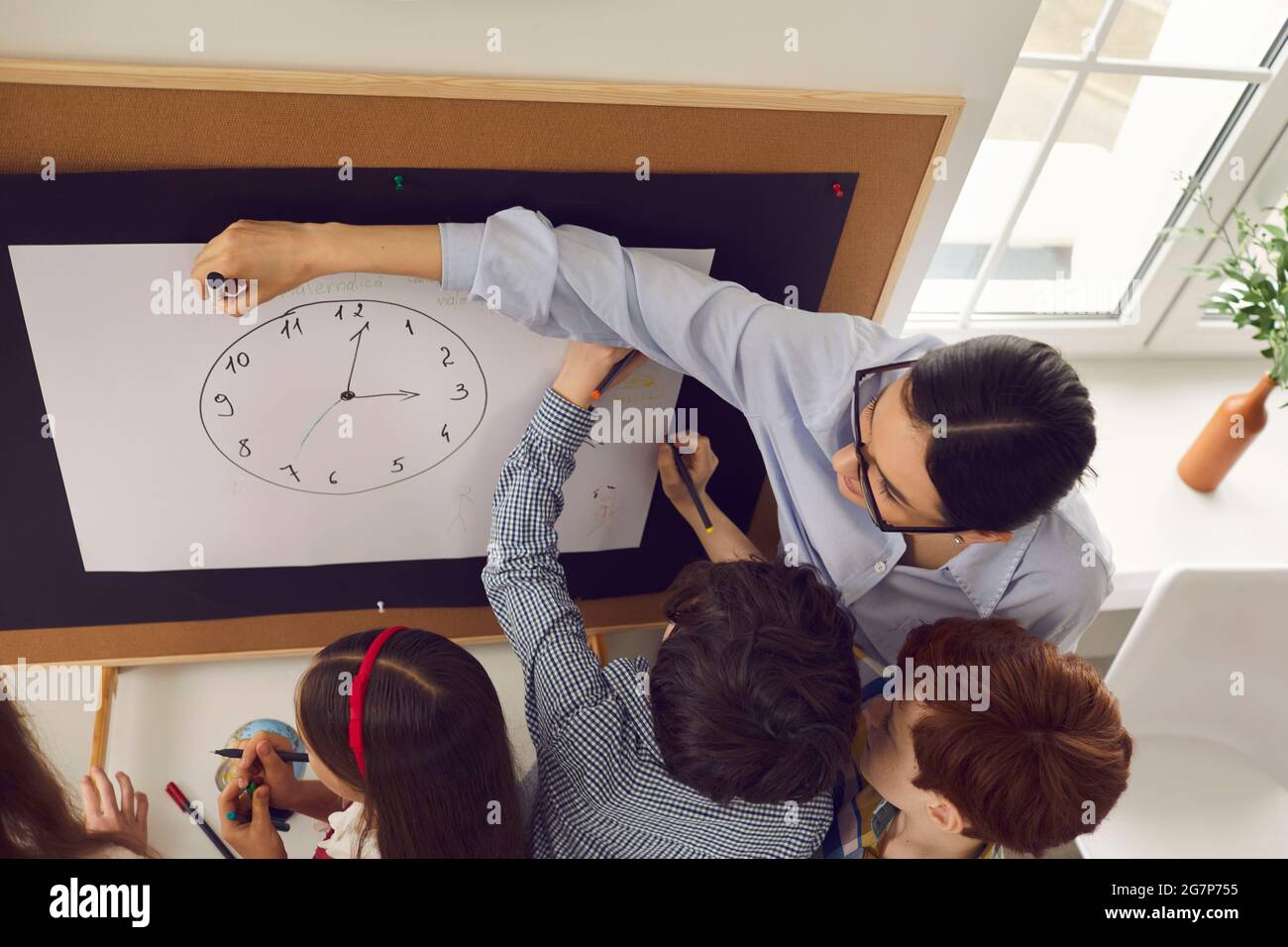 Insegnante femminile che spiega l'ora dell'orologio ai bambini elementari in classe Foto Stock