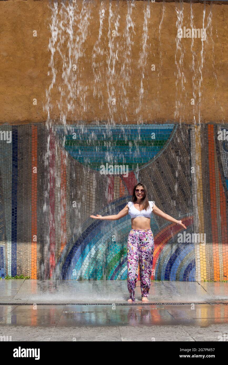 sotto la fontana la ragazza si bagna nel calore Foto Stock