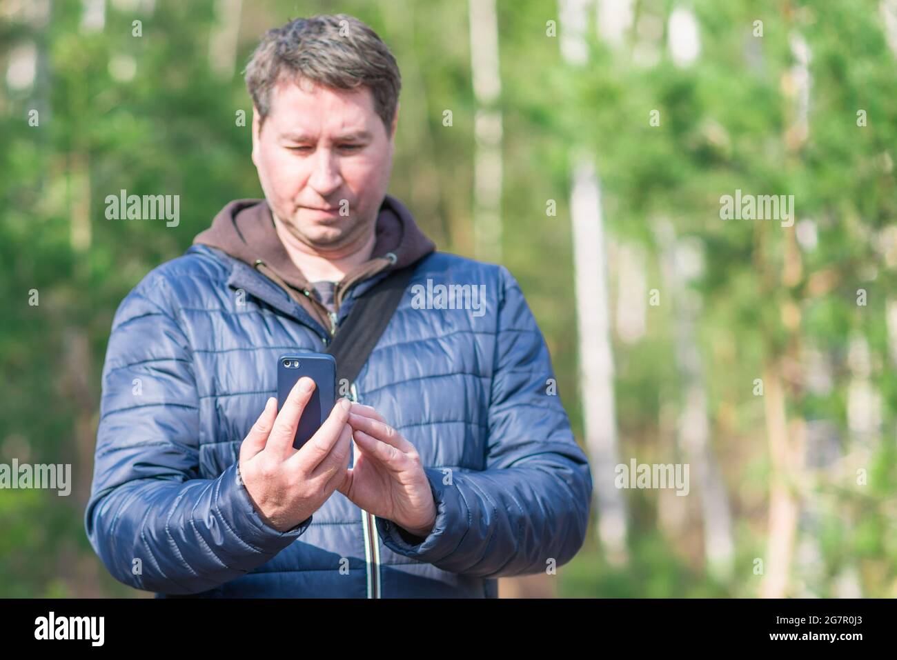 Un uomo di 40 anni con il suo smartphone cellulare alla ricerca del segnale di ricezione nella foresta primaverile. Foto Stock