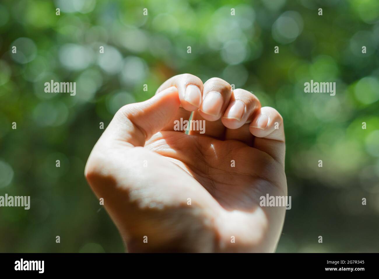 Primo piano concetto esterno di controllo dita unghie mano esposto con luce solare e sfondo verde bokeh Foto Stock