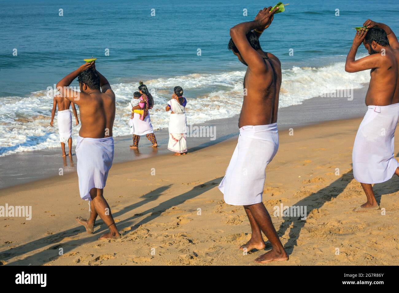 I maschi indiani con castagne nude trasportano offerte di puja per cadere nel Mar Arabico, Varkala, Kerala, India Foto Stock