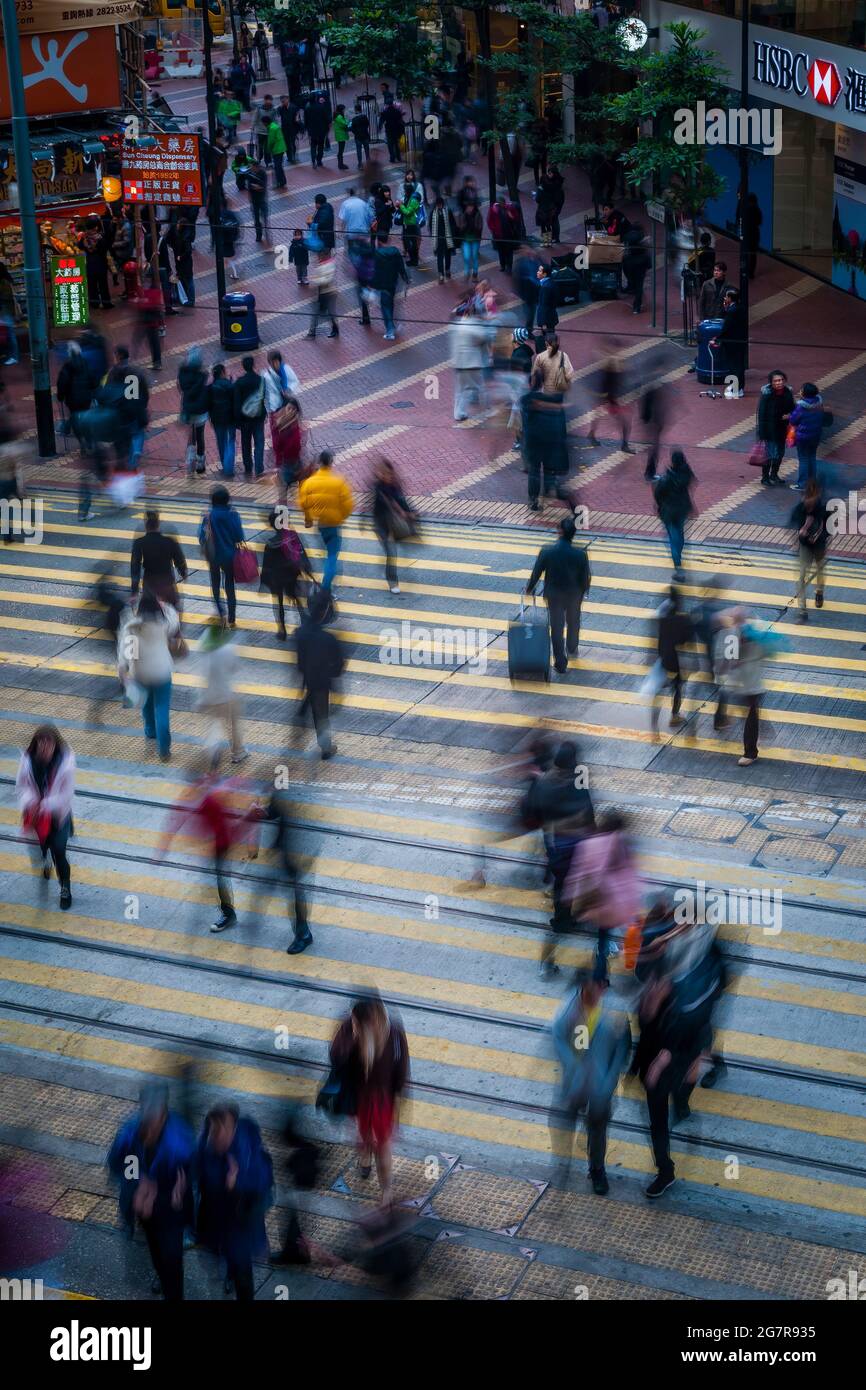 I pedoni attraversano le piste del tram a Causeway Bay, Isola di Hong Kong, con effetto sfocato dalla bassa velocità dell'otturatore Foto Stock