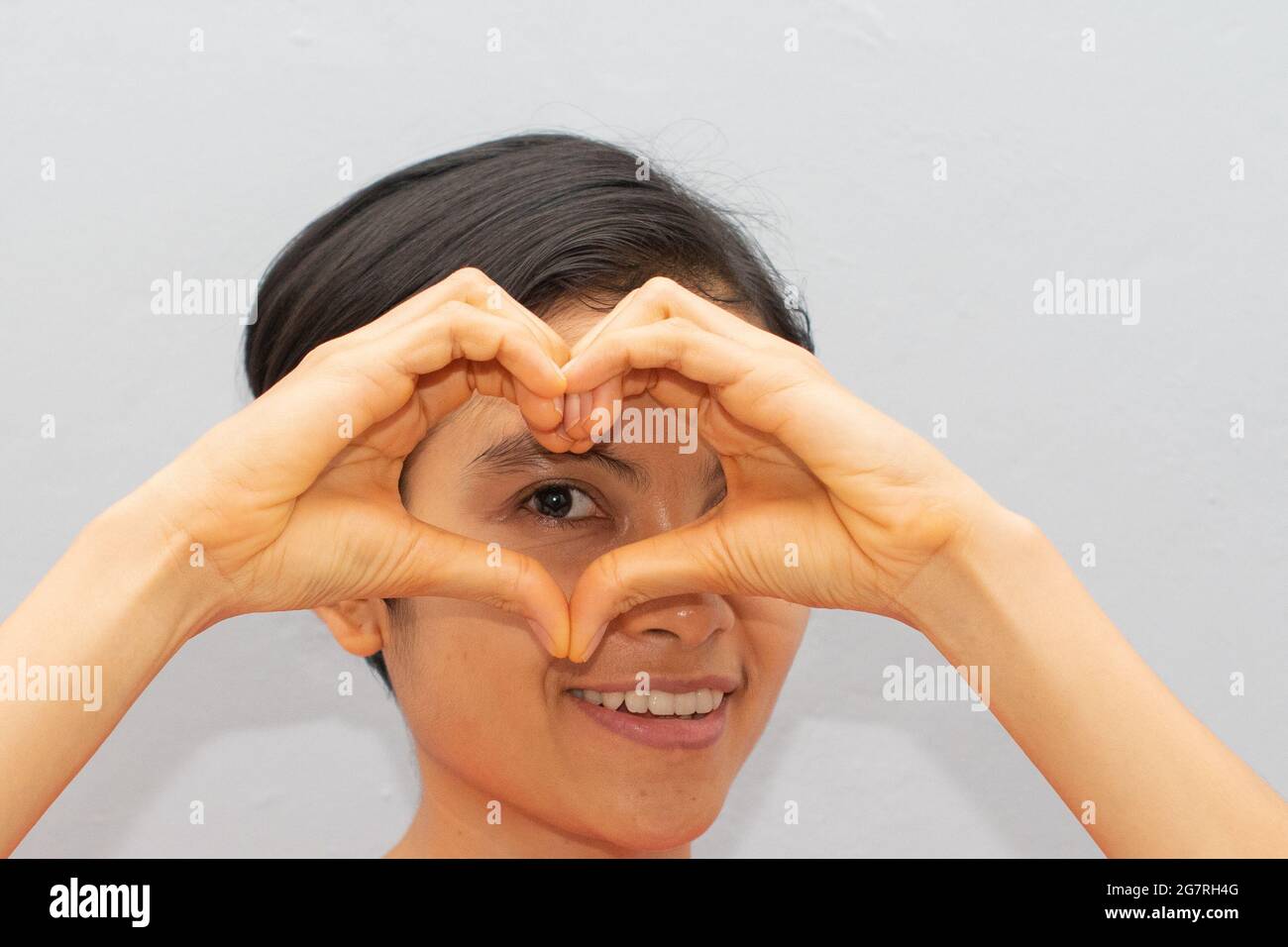 Una giovane donna, capelli corti, bella, sta facendo un segno d'amore con il dito, vicino ai suoi occhi Foto Stock