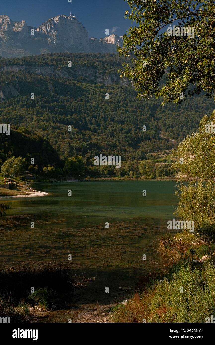 Le tinte autunnali iniziano a comparire a settembre nella fitta foresta e nella fascia di vegetazione acquea che circonda le acque verdi e profonde del lago alpino Molveno, nella regione italiana del Trentino-Alto Adige. Il lago è stato descritto nel 1890 dal poeta e romanziere Antonio Fogazzaro come "la perla preziosa in un caschetto ancora più prezioso". Più recentemente è stato giudicato il lago più bello d'Italia. Il Lago di Molveno, profondo fino a 124 m (406 piedi), ha una foresta pietrificata sul suo letto lacustre che gli scienziati dicono sia stata sommersa per la prima volta circa 3,000 anni fa. Foto Stock