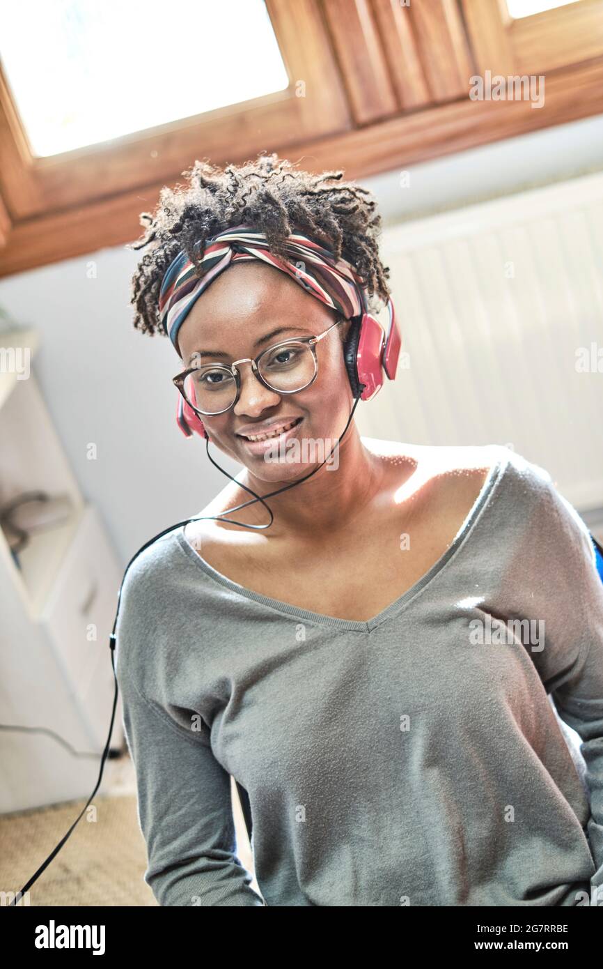 Giovane donna nera con acconciatura afro che ascolta la musica con le cuffie in casa. Concetto di stile di vita. Foto Stock