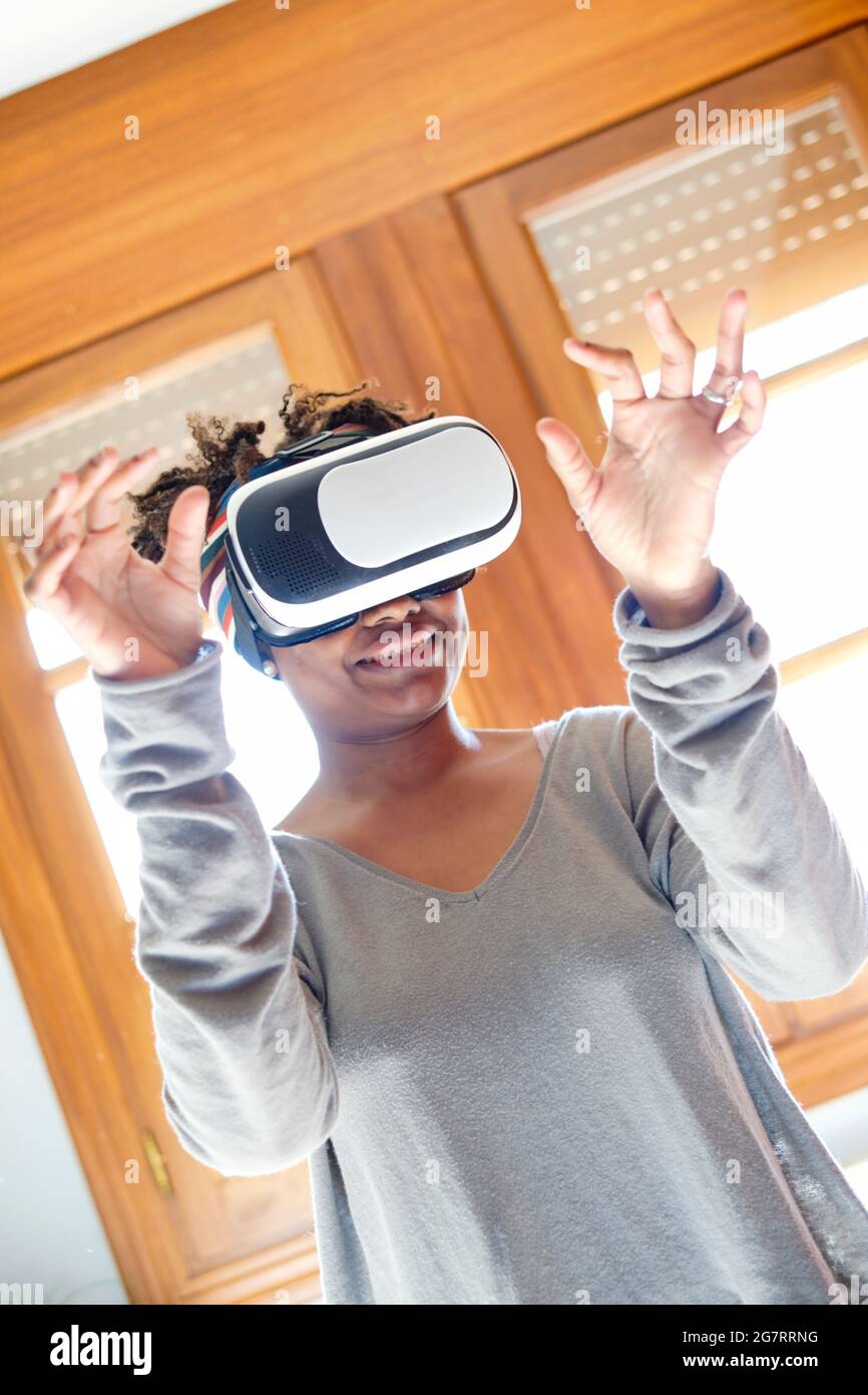 Ritratto di una giovane donna nera attiva che prova un simulatore di realtà virtuale in una stanza a casa. Concetti di tecnologia e stile di vita. Foto Stock