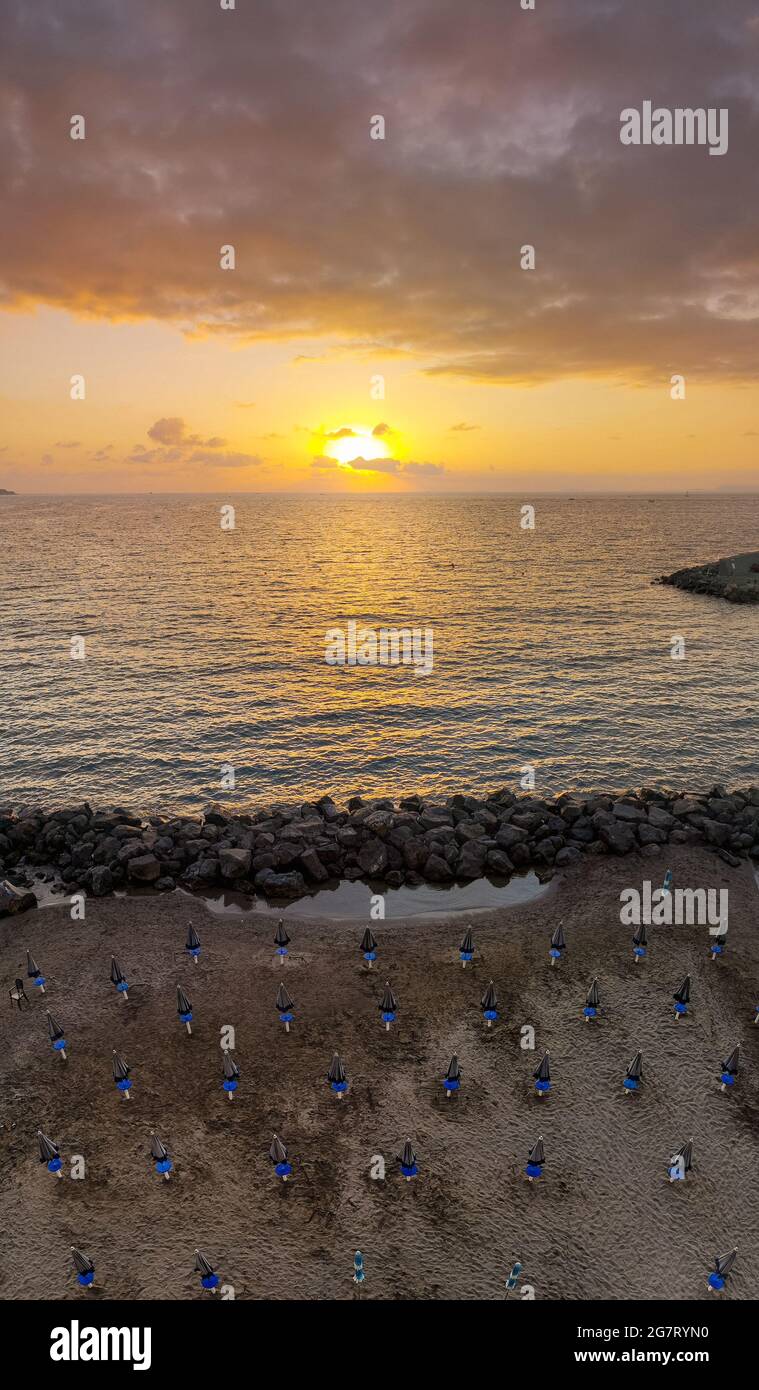 Panorama verticale di bel tramonto sul mare e spiaggia piena di ombrelloni con sole dietro le nuvole Foto Stock