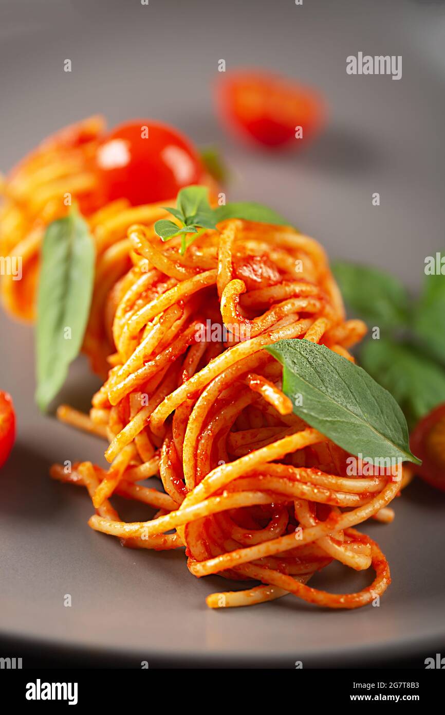 Pasta cotta in un ristorante in salsa di pomodoro con pomodori ciliegini e basilico e servita su un piatto grigio Foto Stock