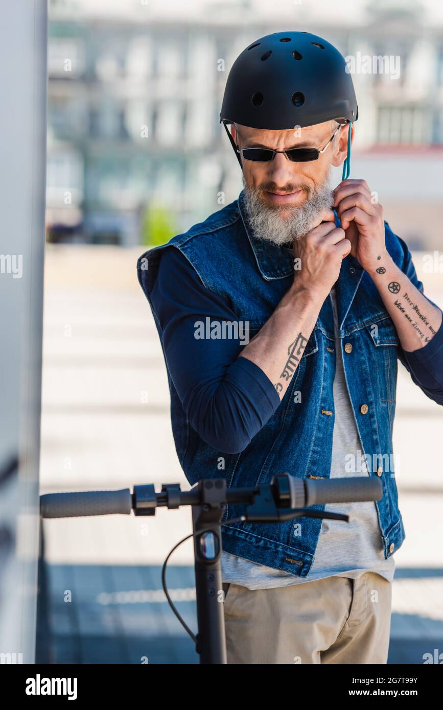 uomo di mezza età tatuato in occhiali da sole con casco vicino scooter  elettrico Foto stock - Alamy