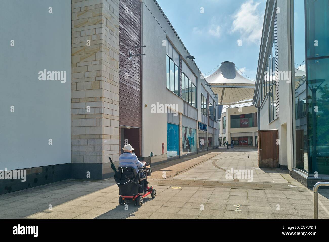 Una persona con disabilità in sedia a rotelle si trova nel complesso commerciale Willow Place nel centro di Corby, Northamptonshire, Inghilterra. Foto Stock