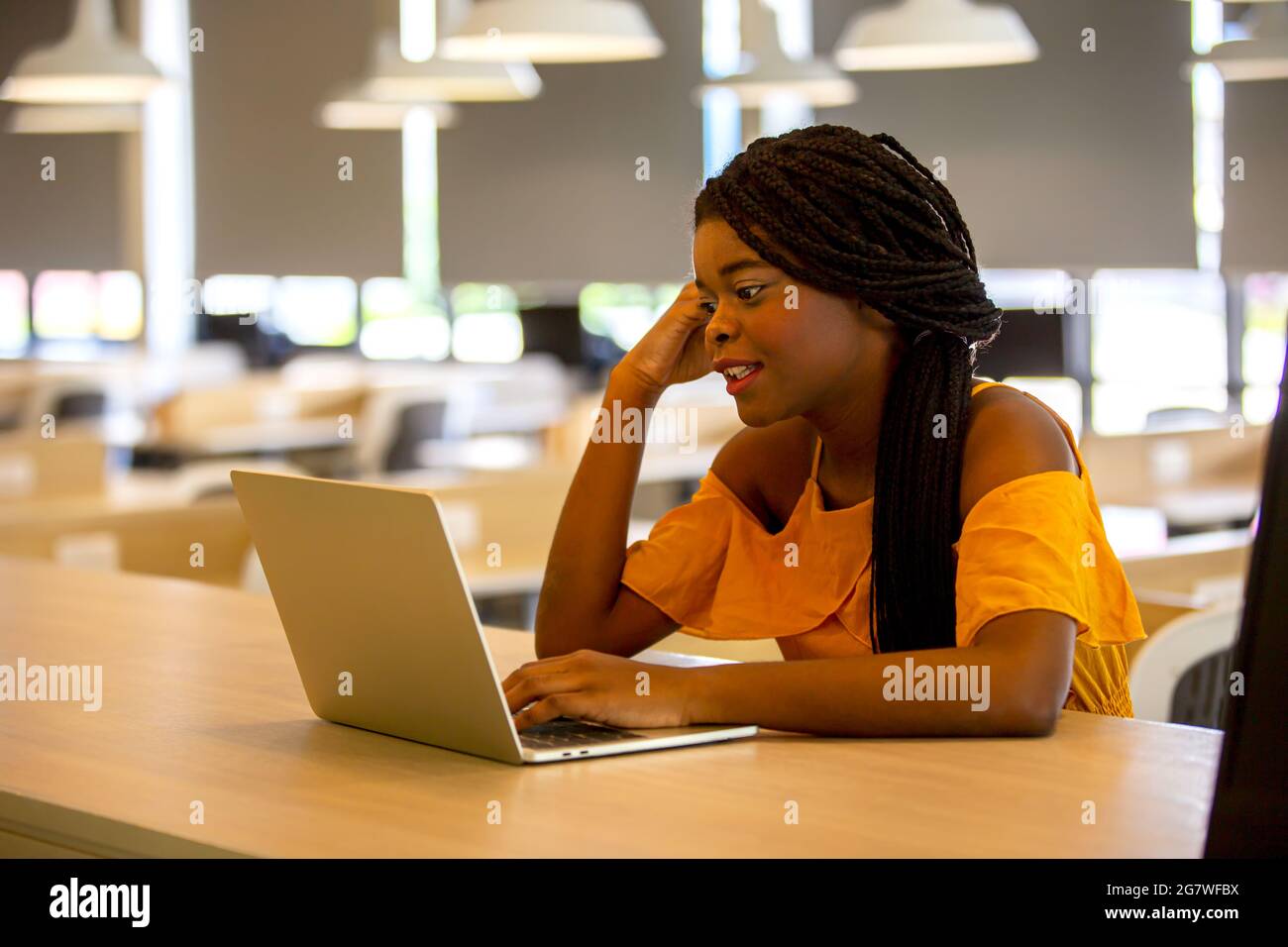 Giovane afroamericana che lavora con computer portatile concentrato e sorridente. Foto Stock