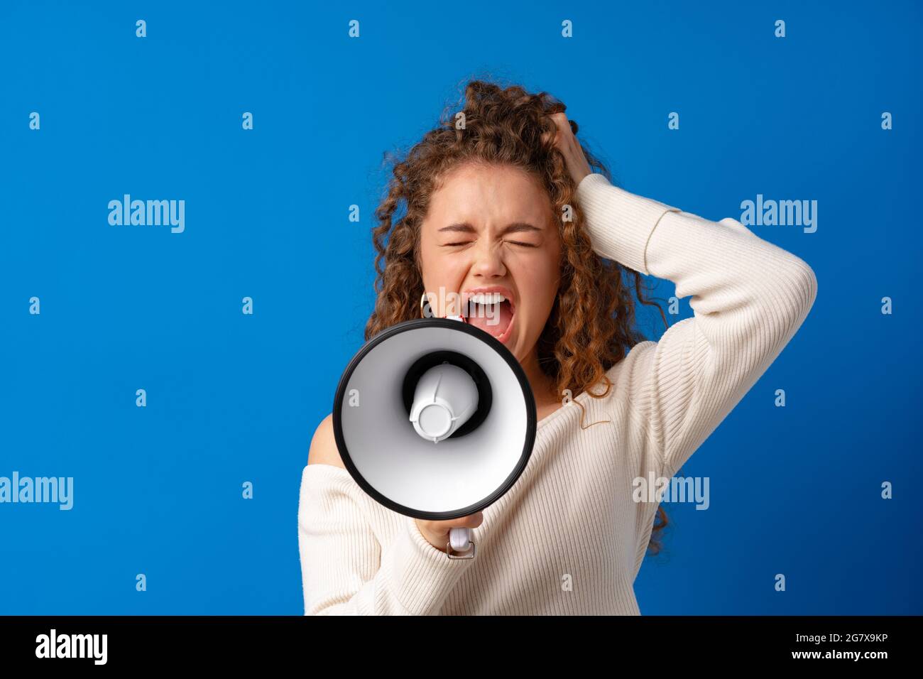 Giovane sorridente espressiva donna caucasica gridò in megafono su sfondo blu Foto Stock