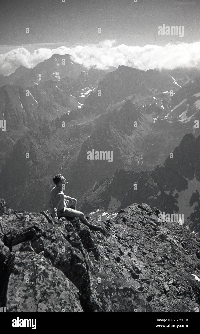 1935, storico, un escursionista maschile seduto su rocce alte sui Sudeti in Cecoslovacchia, che si affaccia sulle catene montuose Sudeten che fanno parte del massiccio della Boemia nell'Europa centrale. Foto Stock