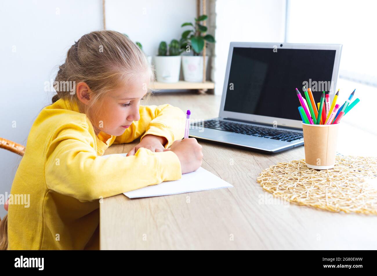 Studentessa caucasica che fa i compiti a casa, scrive in un notebook. Ragazza di 10-11 anni con computer portatile. Scuola domestica, e-learning. Ritorno a scuola. Accogliente Foto Stock