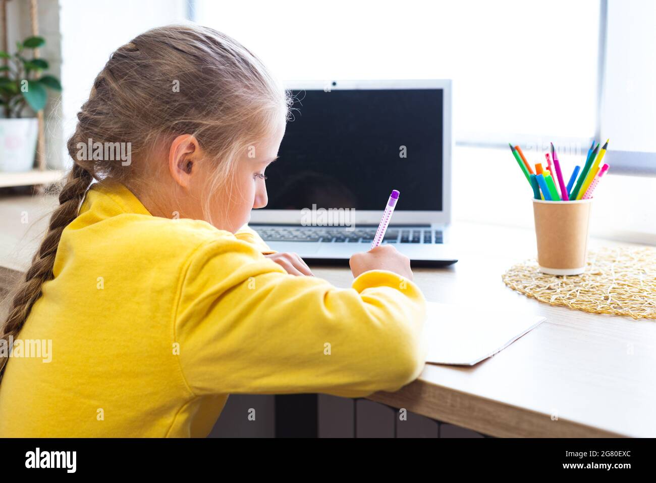 Studentessa caucasica che fa i compiti a casa, scrive in un notebook. Ragazza di 10-11 anni con computer portatile. Scuola domestica, e-learning. Ritorno a scuola. Accogliente Foto Stock