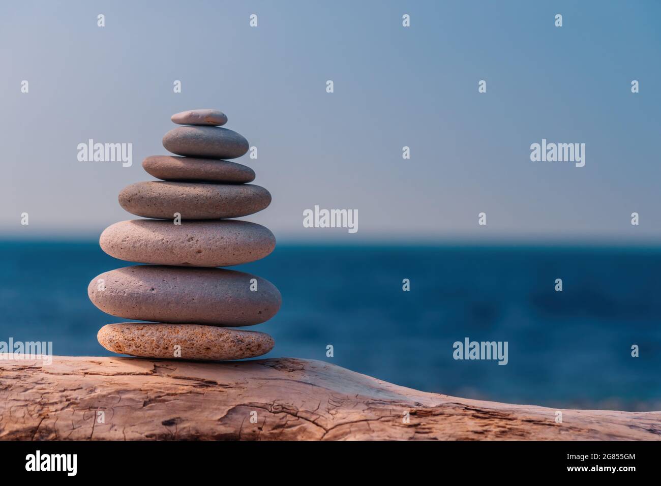 Equilibrata piramide di ciottoli sulla spiaggia in una giornata di sole. Abstract Sea bokeh sullo sfondo. Messa a fuoco selettiva. Pietre Zen sulla spiaggia di mare, meditazione Foto Stock