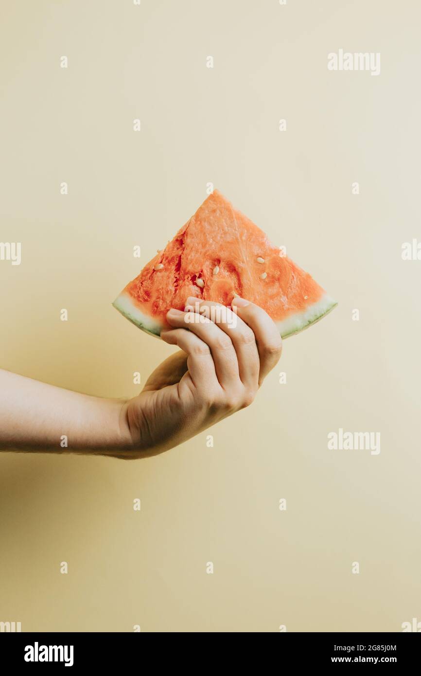 Una mano che tiene una fetta di anguria contro uno sfondo giallo con spazio di copia - concetto estivo Foto Stock