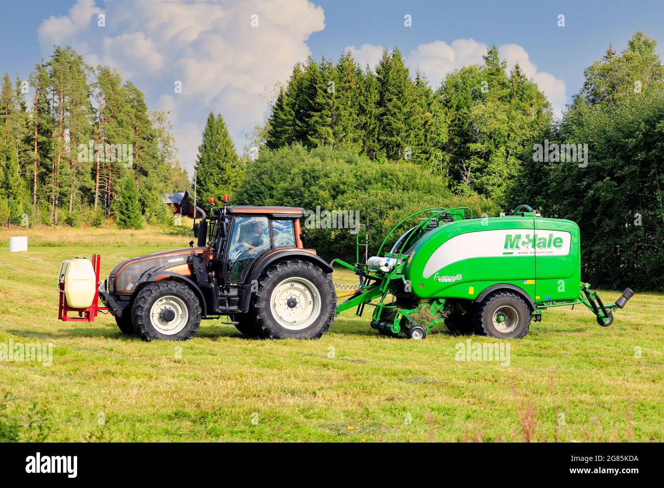 Coltivatore che lavora nel campo del fieno con il trattore Valtra e McHale 3 più il legatore integrato dell'imballatrice. Salo, Finlandia. 28 agosto 2020. Foto Stock