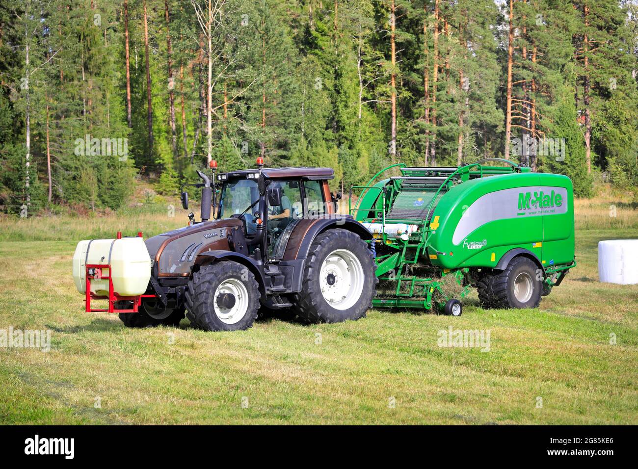 Coltivatore che lavora nel campo del fieno con il trattore Valtra e McHale 3 più il legatore integrato dell'imballatrice. Salo, Finlandia. 28 agosto 2020. Foto Stock