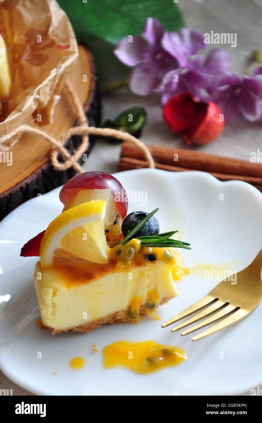 Primo piano UN pezzo di Cheesecake di New York con frutta estiva e salsa alla frutta della passione su piatto bianco Foto Stock