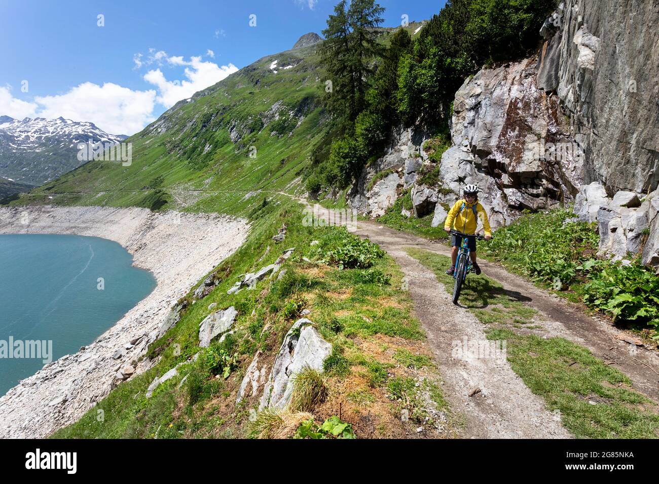 Ragazzo su una mountain bike in bicicletta su una strada di ghiaia lungo il lago artificiale di Kölnbreinsperre alla fine della valle di Malta, in Austria Foto Stock