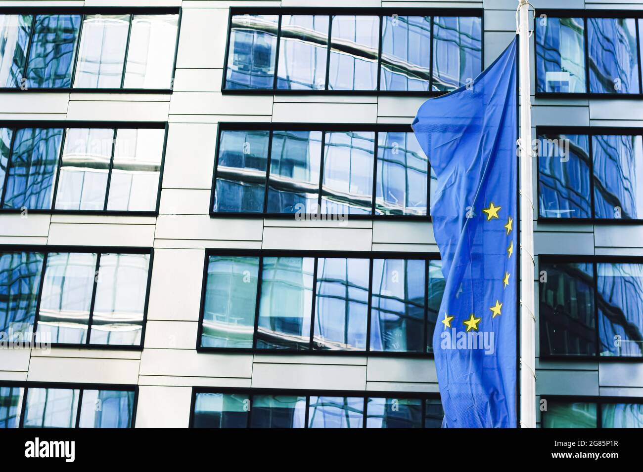 Bandiera dell'Unione europea che sventola di fronte al moderno edificio degli uffici aziendali, simbolo del Parlamento europeo, della Commissione e del Consiglio Foto Stock