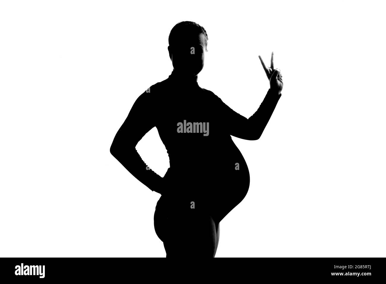 Giovane donna incinta che mostra due dita, positivo o gesto di pace Foto Stock