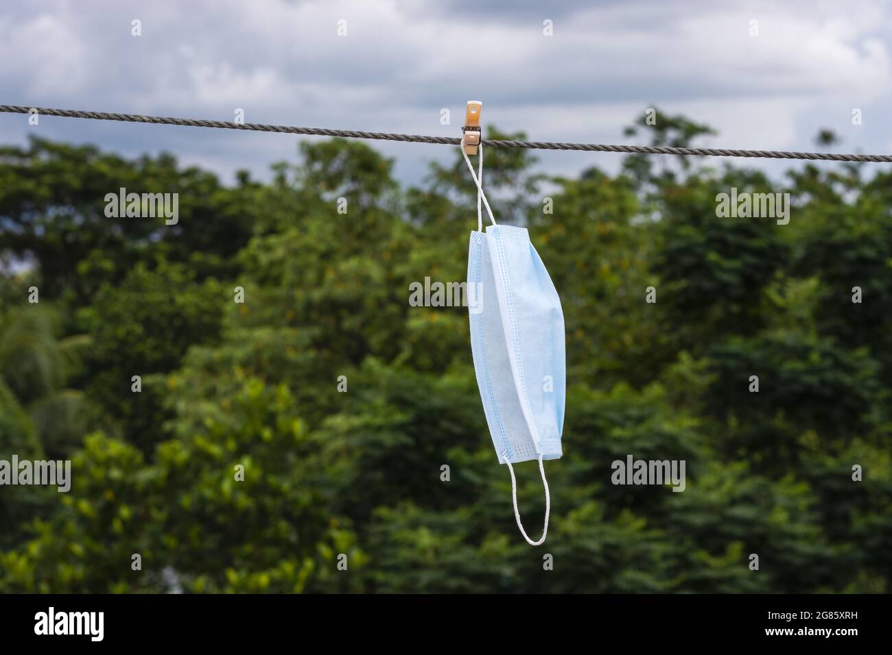 Una maschera chirurgica bagnata appesa con un panno per asciugare al sole Foto Stock