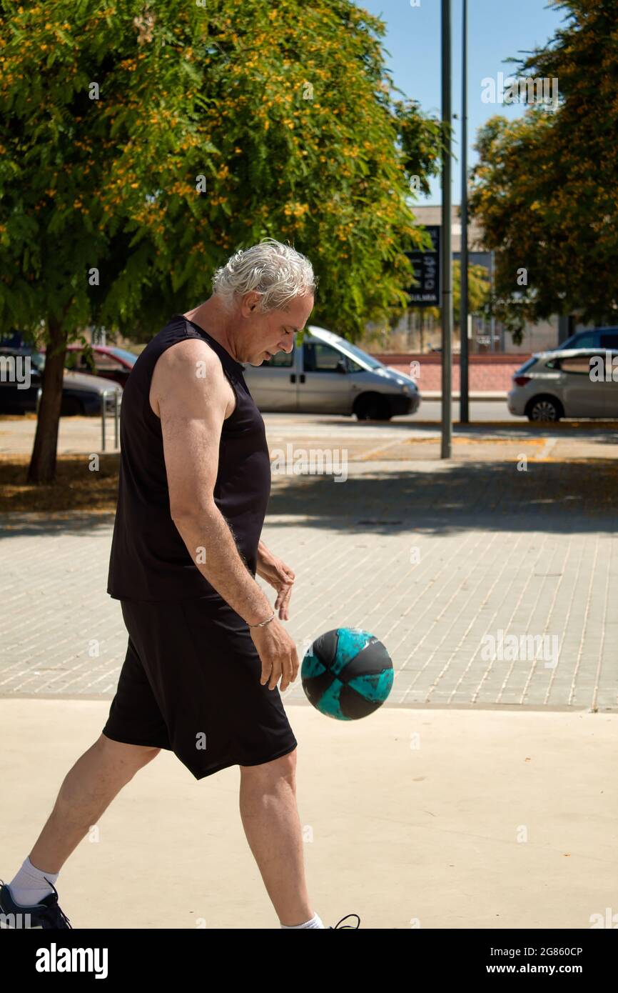 uomo maturo che gioca a basket da solo su un campo di strada con cesto di metallo Foto Stock