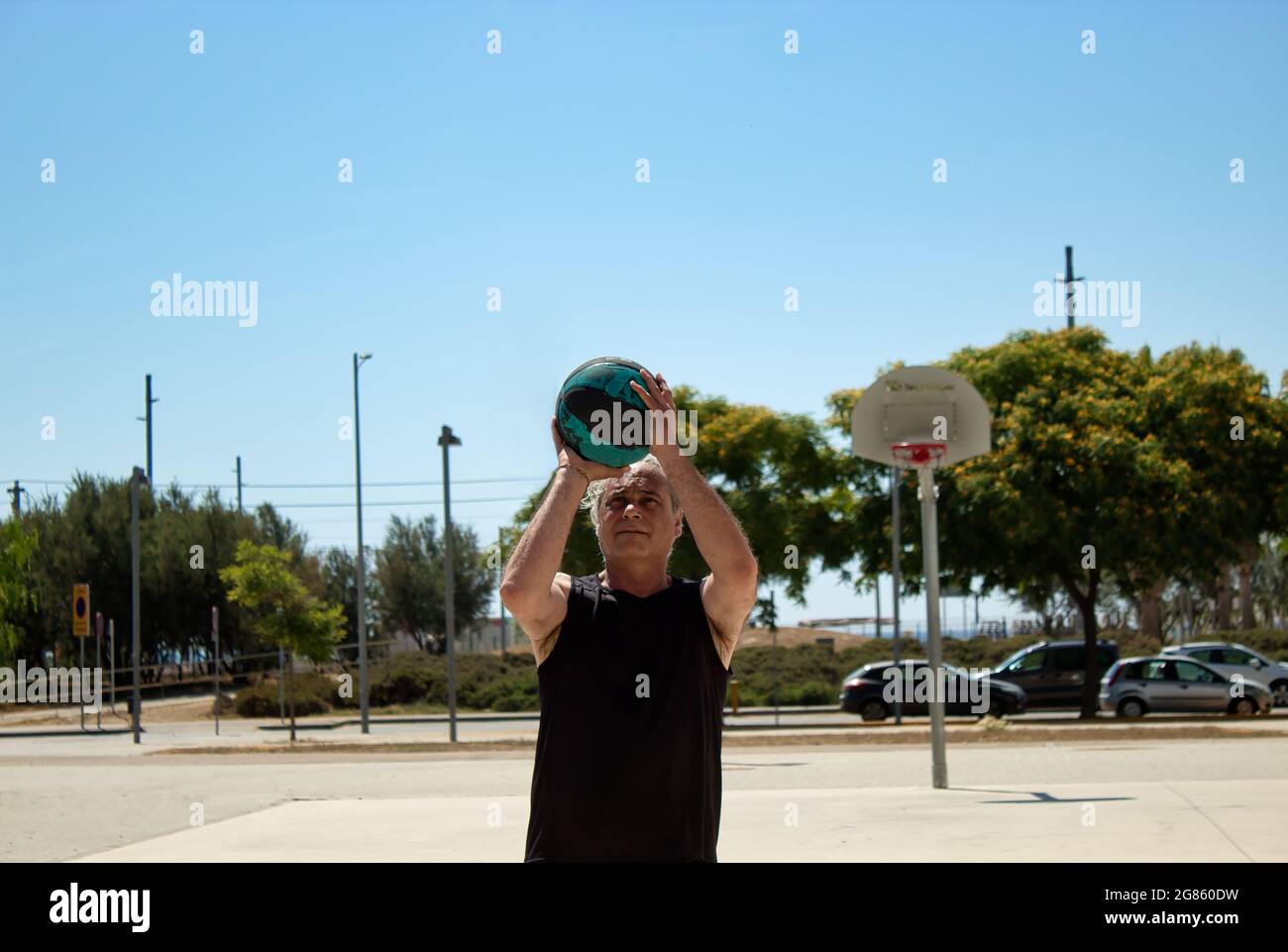 uomo maturo che gioca a basket da solo su un campo di strada con cesto di metallo Foto Stock