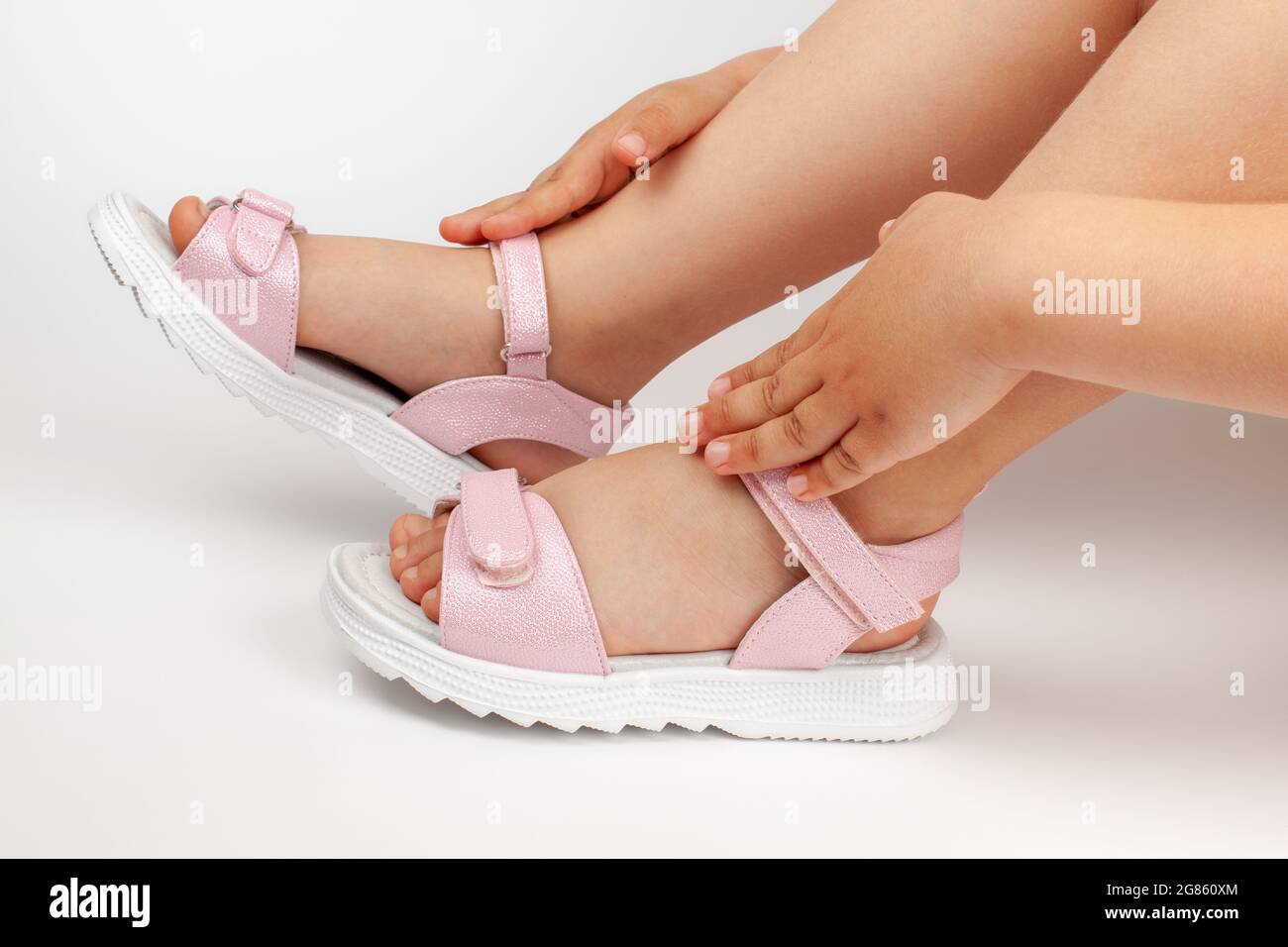 macro dettagli sandali rosa per bambini sui piedi della ragazza di un bambino seduto su uno sfondo bianco versato Foto Stock