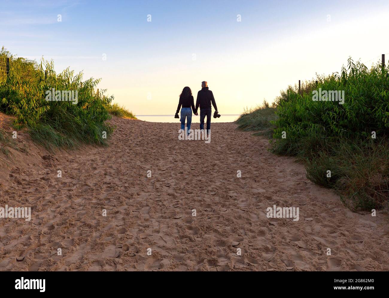 Un paio di amanti camminano lungo la spiaggia di sabbia tenendo le mani. Swinoujscie. Pomerania. Polonia. Foto Stock