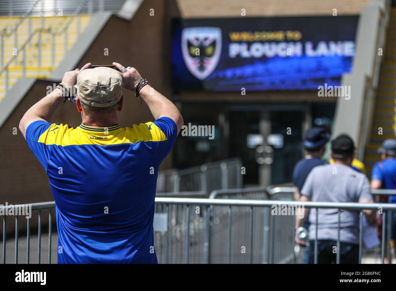 Un sostenitore dell'AFC Wimbledon scatta una foto fuori terra prima della partita pre-stagione a Plough Lane, Londra. Foto Stock