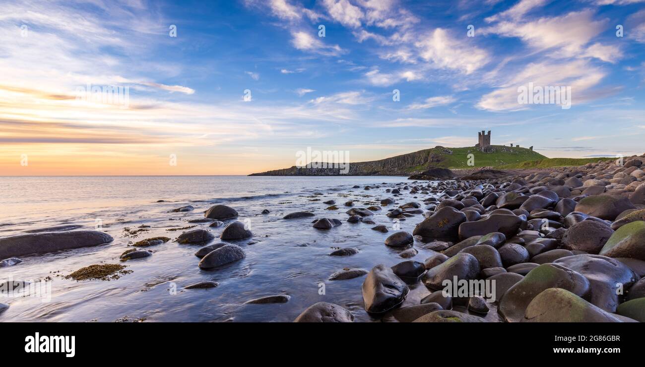 Castello di Dunstanburgh all'alba da Embleton Bay sulla costa del Northumberland, Inghilterra, Regno Unito Foto Stock