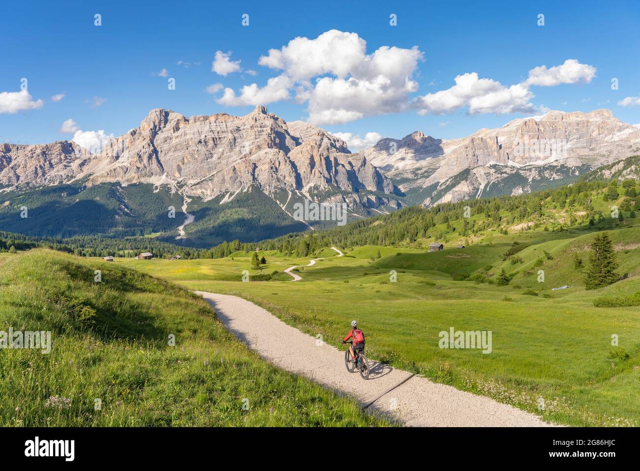 Bella e attiva donna anziana che cavalca la sua mountain bike elettrica sull'altopiano di Pralongia, nelle Dolomiti dell'alta Badia, con l'impressionante Sasso die Santa Cruce Foto Stock