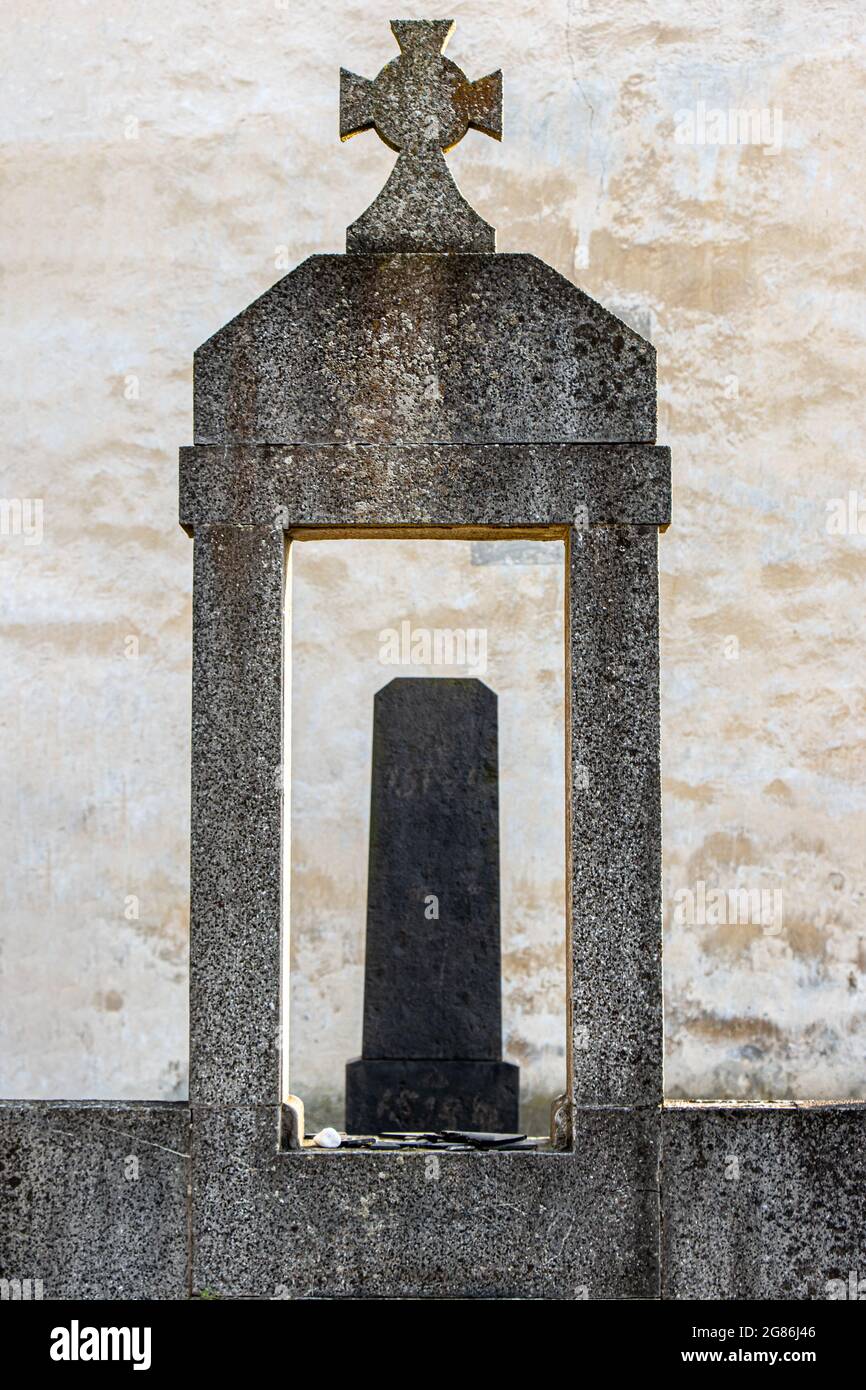 Una lapide danneggiata con una croce e emblema nel cimitero Foto Stock