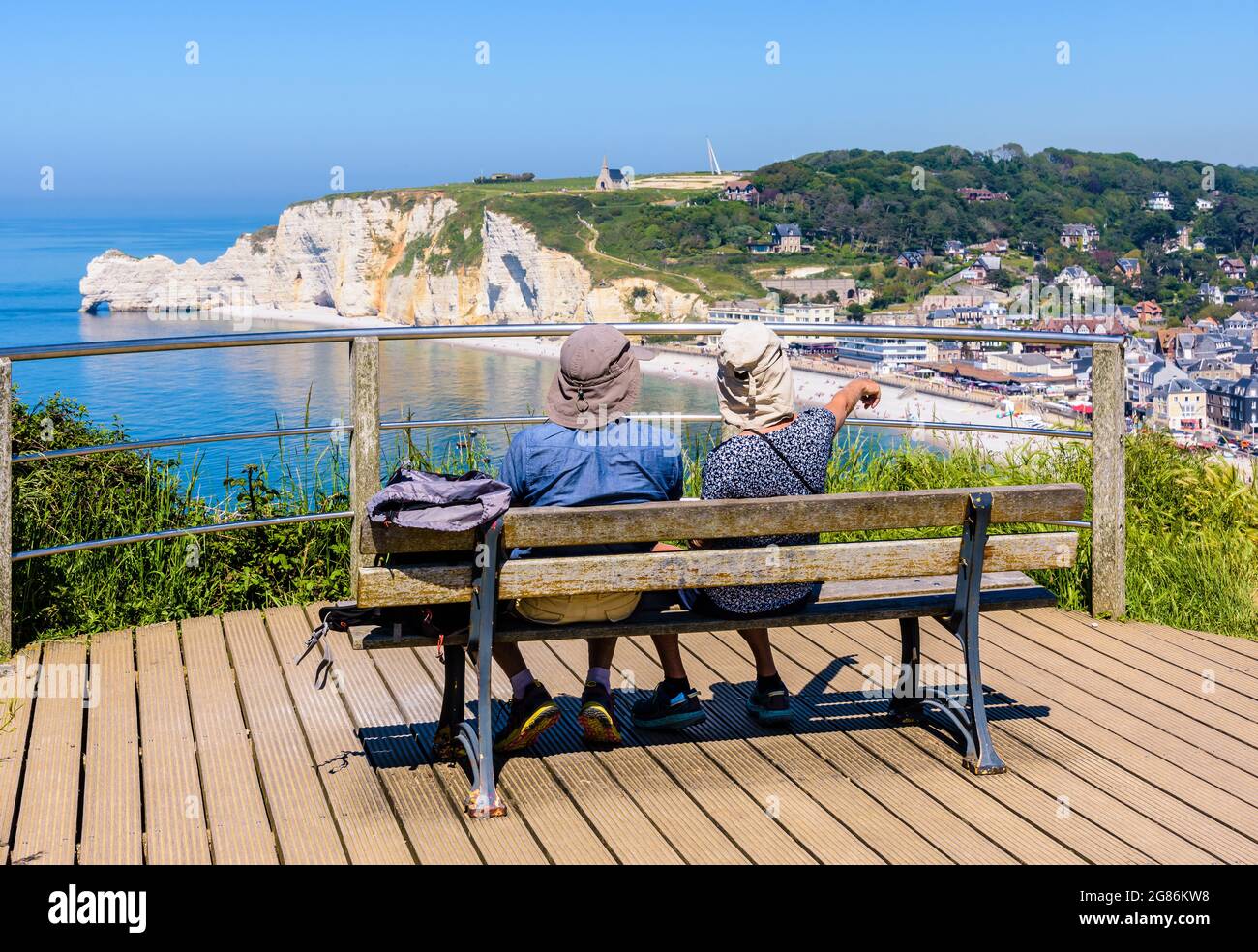 Un paio di escursionisti seduti su una panchina gode di una vista panoramica sulla città balneare di Etretat e sulla scogliera di Amont in Normandia in una giornata di sole. Foto Stock