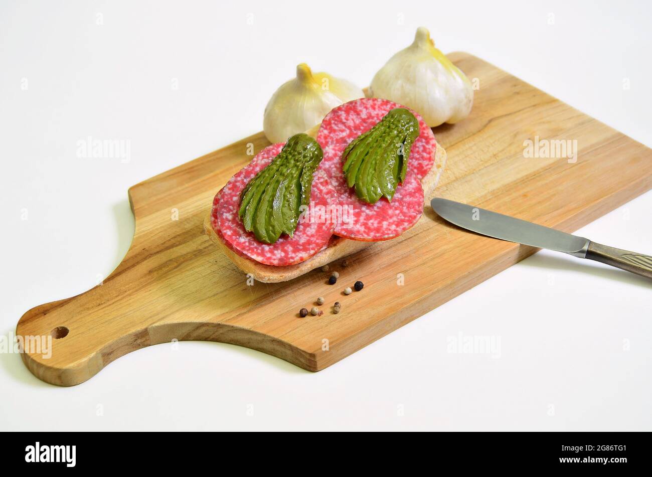 sandwich di salame con gherkin e aglio sottaceto su tagliere, primo piano, isolato su sfondo bianco Foto Stock