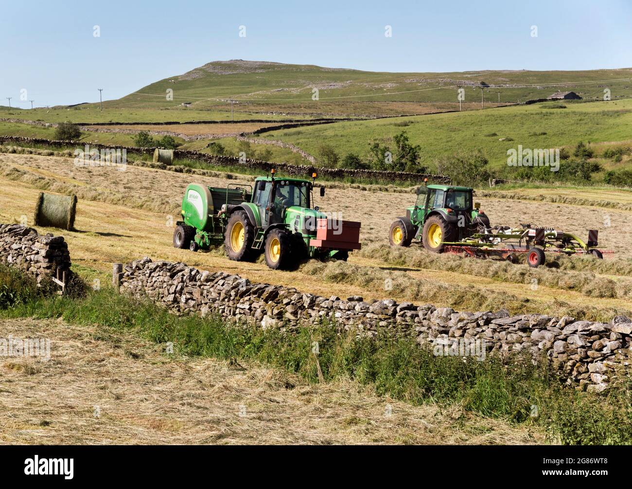 Haymaking estivo, Helwith Bridge, Yorkshire Dales National Park, Regno Unito. Macchine tornitura e rotoimballaggio fieno. Foto Stock