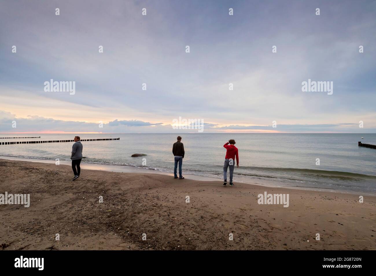 Tre persone tornano alla lente in piedi sulla riva del mare di Ost durante il tramonto nuvoloso Foto Stock