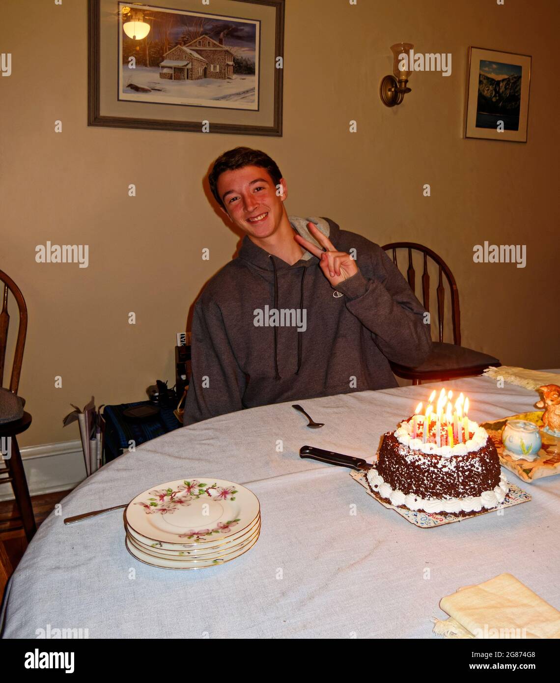teen boy, festeggiando il compleanno, torta, candele accese, seduto a tavola, occasione speciale, fare segno di pace, bello, sorridente, felice, SIGNOR Foto Stock