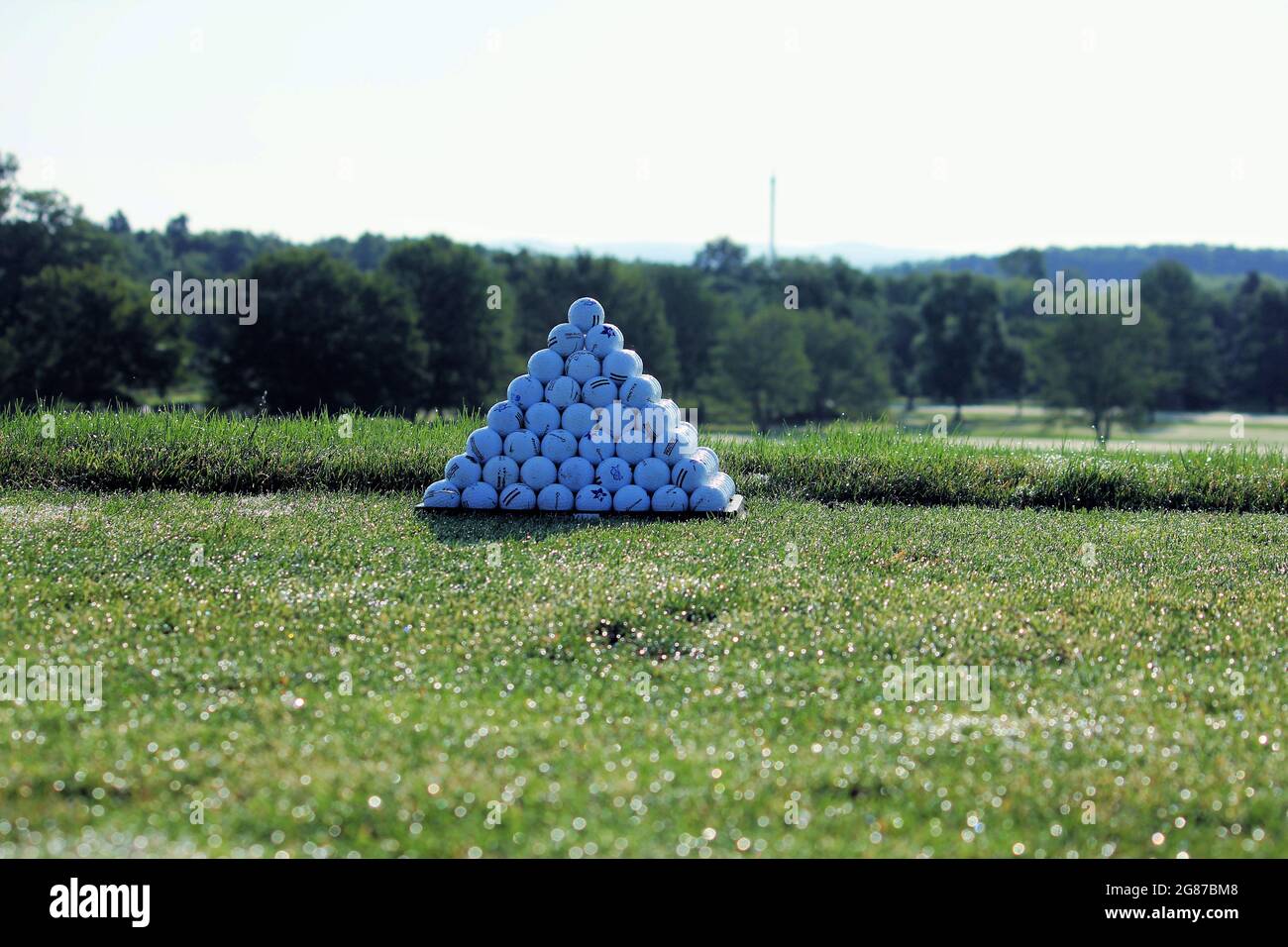 Una piramide solistica di palline da golf al mattino contro uno sfondo verde alberato Foto Stock