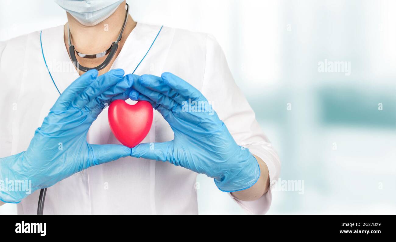 Medico che tiene un cuore rosso presso l'ufficio dell'ospedale. Medicina e concetto di salute, amore di sanità, dare, speranza e concetto di famiglia. Foto Stock