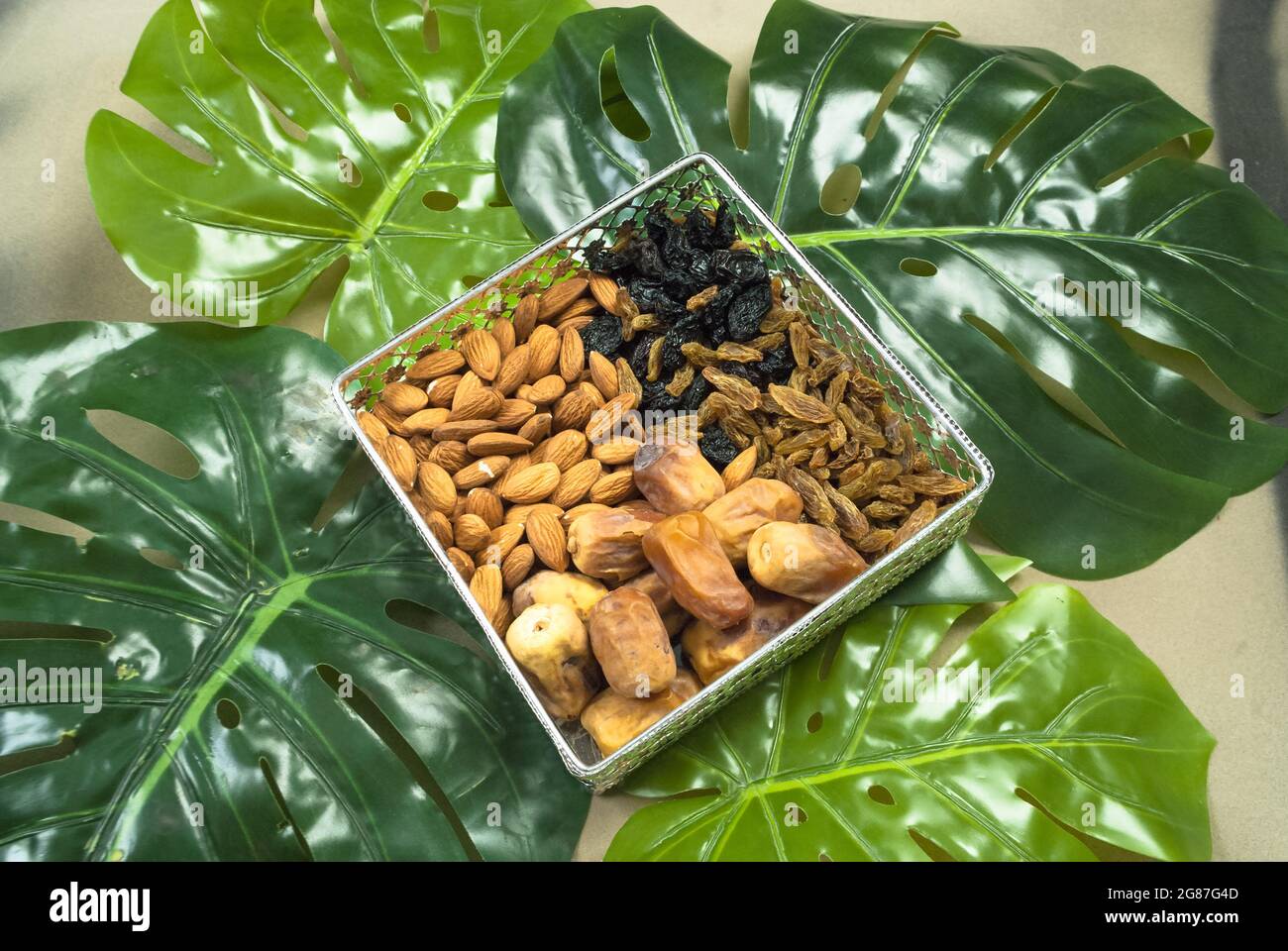 cibo sano organico in ciotola su foglie tropicali, diverse mandorle di frutta secca date uva secca nera dorata (kishmish) dieta jim Foto Stock