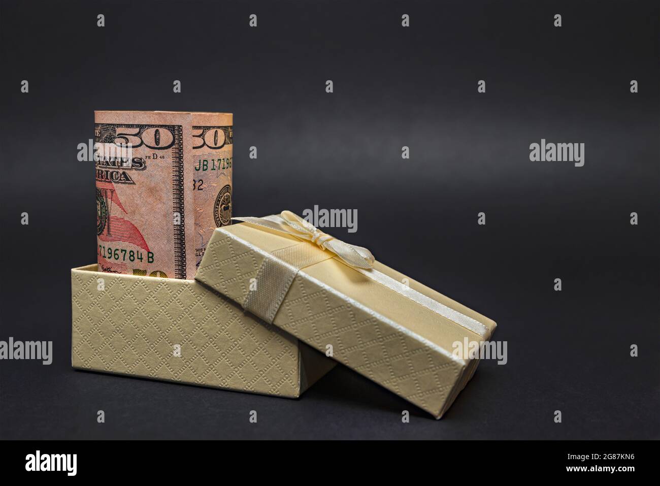 Soldi come regalo. Un dollaro in una scatola con un arco, su uno sfondo nero omogeneo. Inserire il testo. Foto Stock