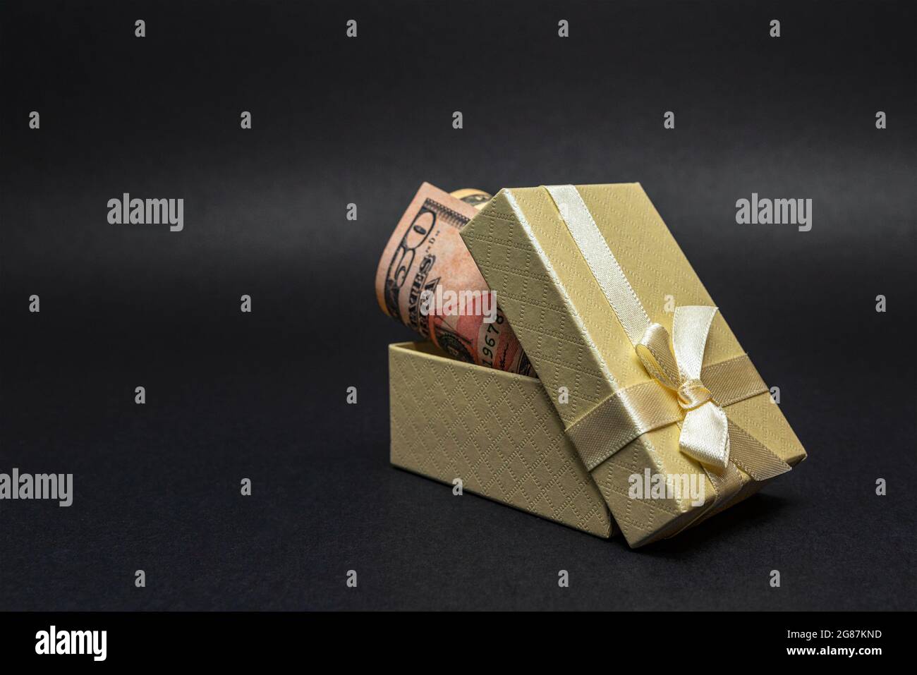 Soldi come regalo. Un dollaro in una scatola con un arco, su uno sfondo nero omogeneo. Inserire il testo. Foto Stock