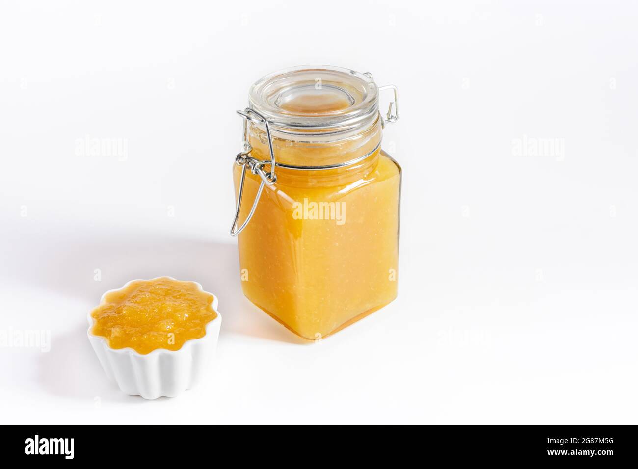 Inceppamento giallo su sfondo bianco. Frutta in casa confiture in un vaso e un closeup ciotola. Spazio di copia. Foto Stock