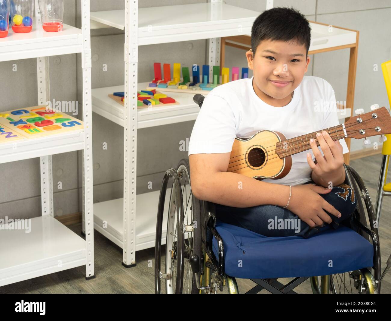 Ritratto di bambino disabile in una sedia a rotelle sta giocando l'ukulele in attività sensoriale. Concetto di apprendimento dei bambini disabili a scuola. Foto Stock