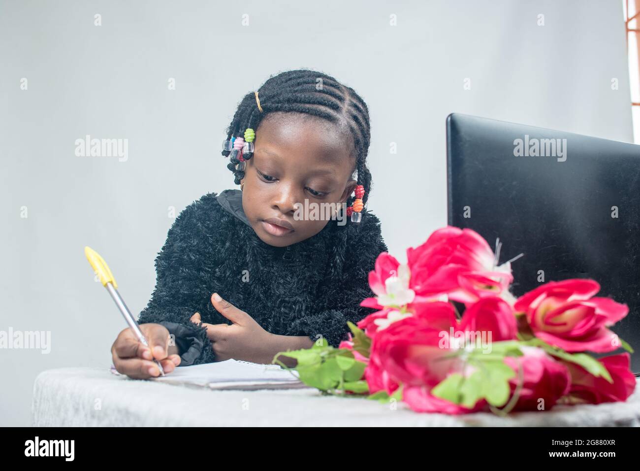 Bambina africana che studia, impara, legge e studia da sola per l'eccellenza nella sua educazione con un laptop, un fiore e una jotter davanti Foto Stock