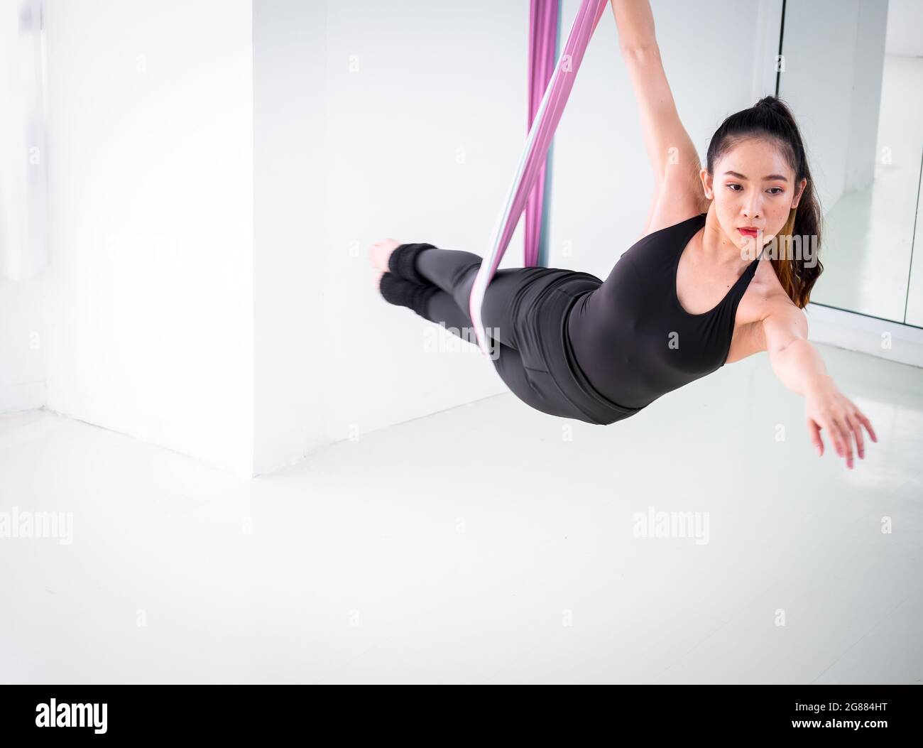 Giovane ballerina asiatica vestita di danza aerea di colore nero con tessuti multicolore nello studio. Foto Stock